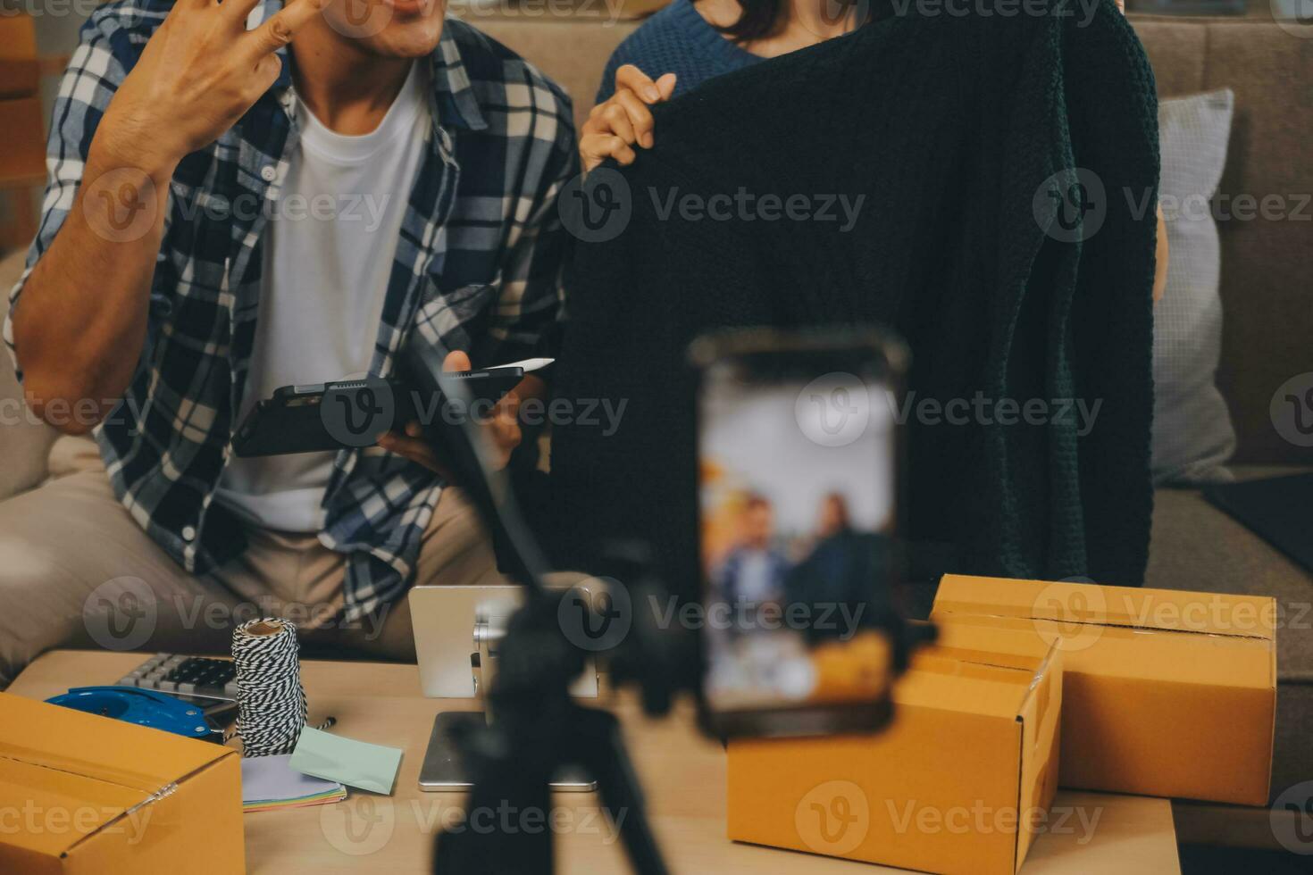 Two Asian blogger showing clothes in front of the camera to recording vlog video live streaming at her shop. Online Shopping Cart notion. on sofa at home photo