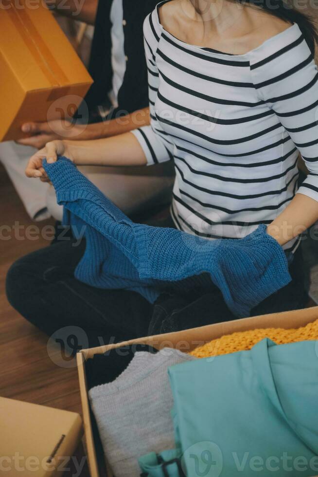 Two Asian blogger showing clothes in front of the camera to recording vlog video live streaming at her shop. Online Shopping Cart notion. on sofa at home photo