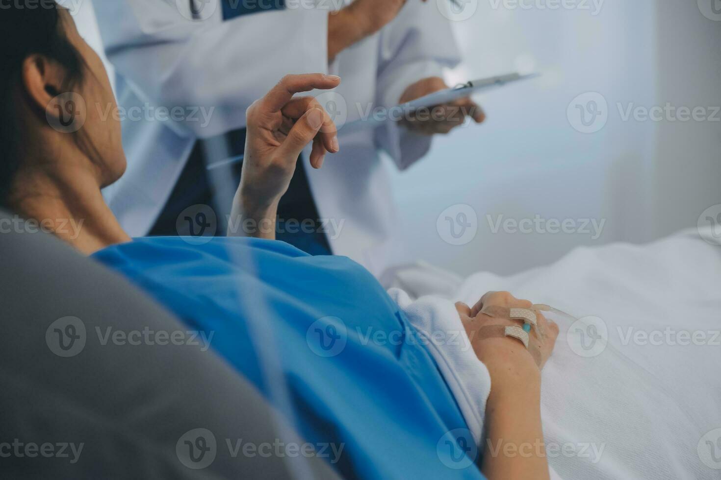 The senior woman specialist doctor with stethoscope checking up happy young Asian female patient lying in bed with receiving an intravenous saline drip in recovery room. Healthcare, medical insurance. photo