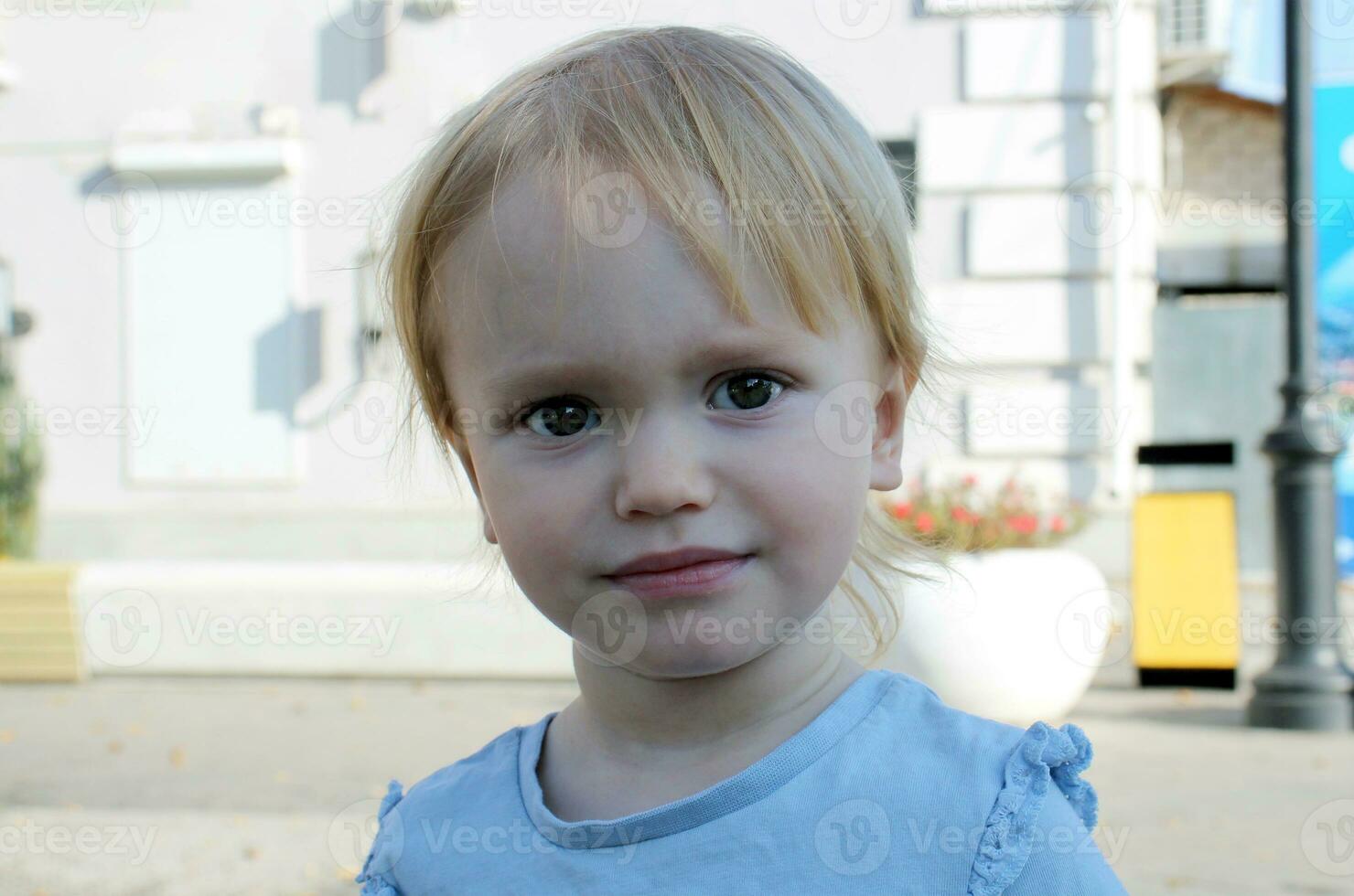 Portrait of a 2 year old blond girl on a background of leaves. Caucasian todler with big eyes looks at the camera and smiles. photo