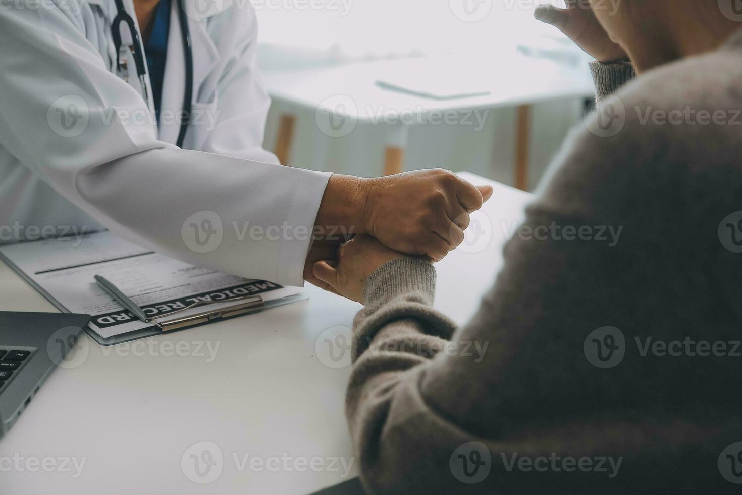 Doctor and patient sitting near each other at the table in clinic office. The focus is on female physician's hands reassuring woman, only hands, close up. Medicine concept photo