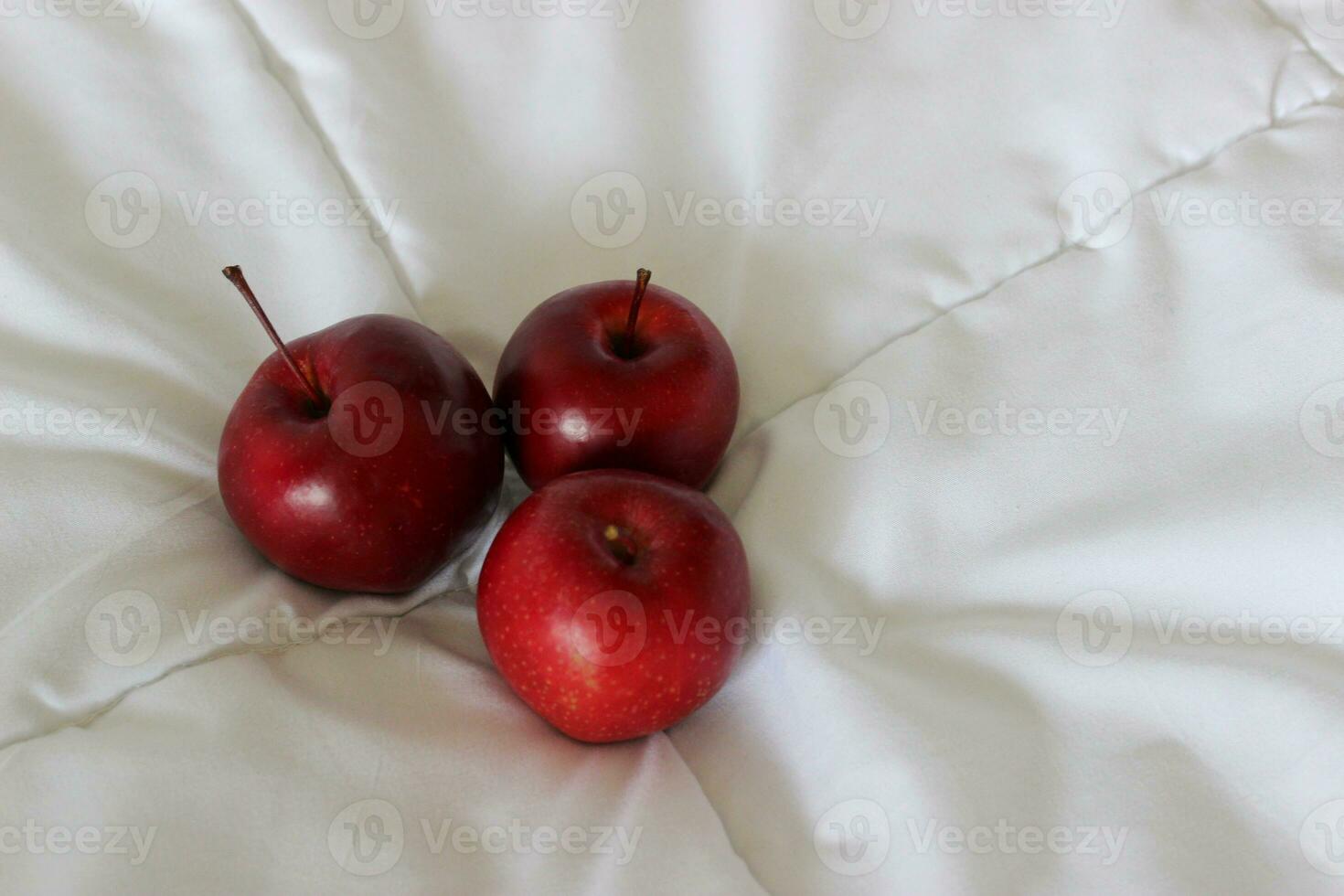Three red ripe apple fruits on a quilted blanket at a side of image concept for logo or titles photo