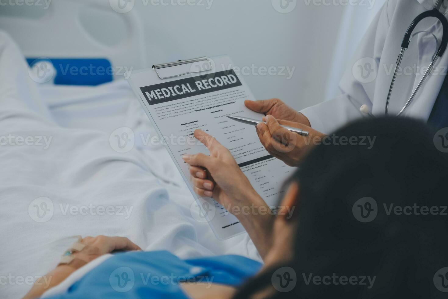 The senior woman specialist doctor with stethoscope checking up happy young Asian female patient lying in bed with receiving an intravenous saline drip in recovery room. Healthcare, medical insurance. photo