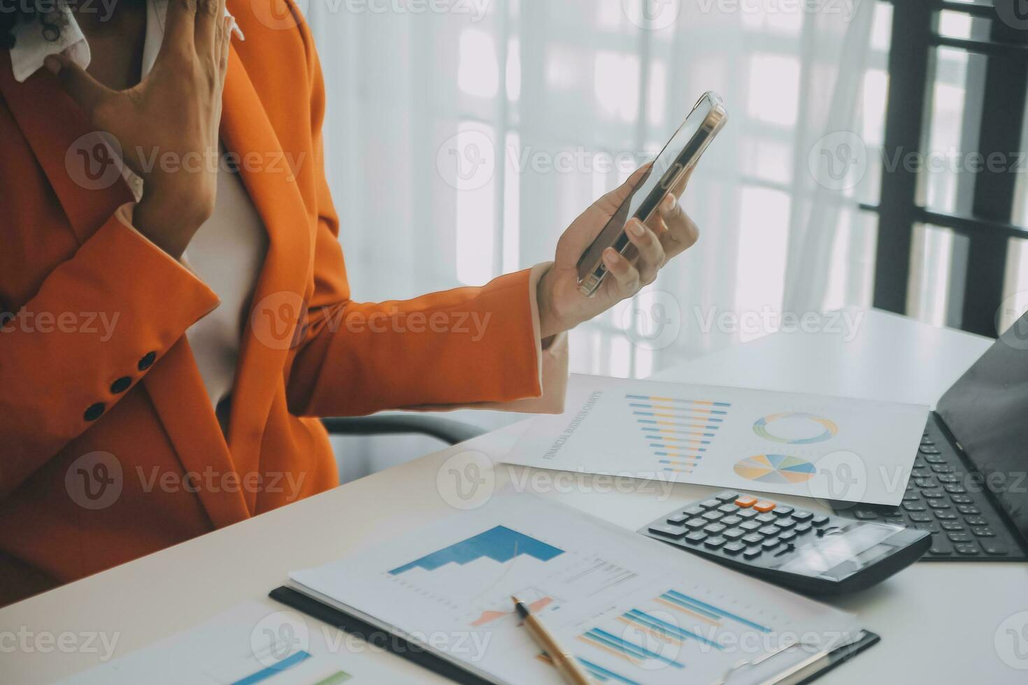 Smiling young Asian businesswoman working on a laptop computer at her desk in a bright modern home office, doing calculating expense financial report finance making notes on paper graph data document. photo