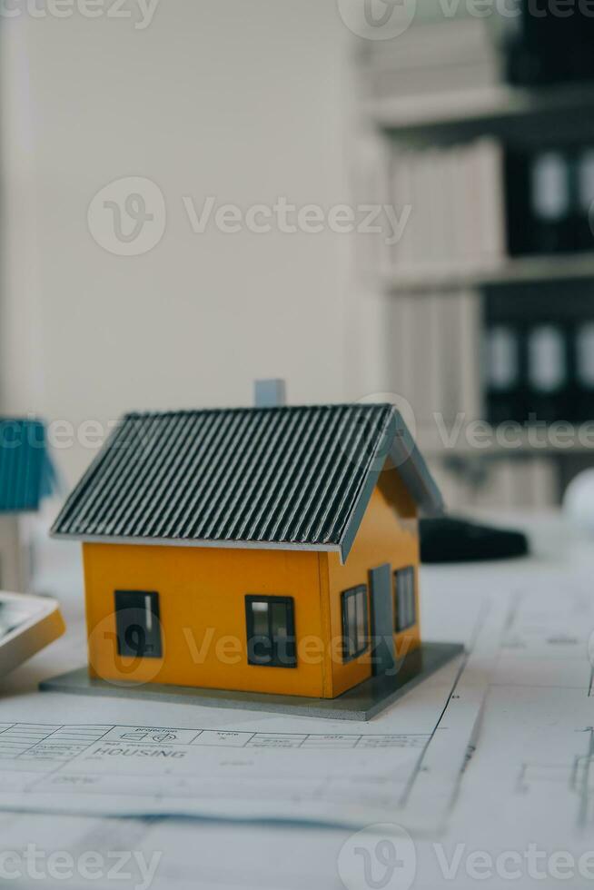 architectural model of houses on desk with drawing technical tools and blueprint rolls, isolated on white background, for building construction plan, interior designer and architect work concept photo