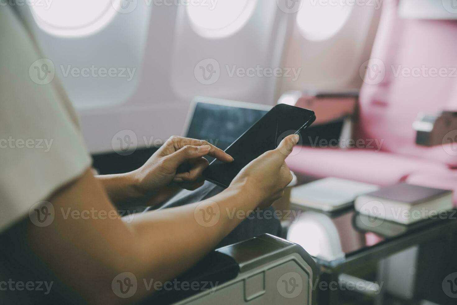 Asian woman passenger sitting in airplane near window and reading news from social networks or using travel applications in smartphone photo