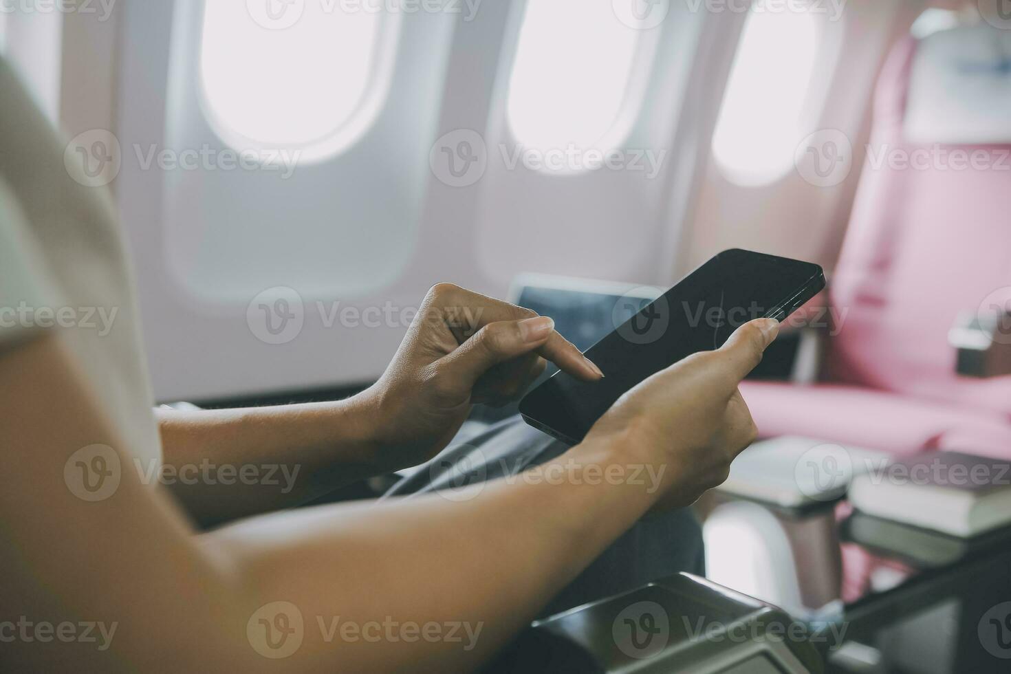 Asian woman passenger sitting in airplane near window and reading news from social networks or using travel applications in smartphone photo