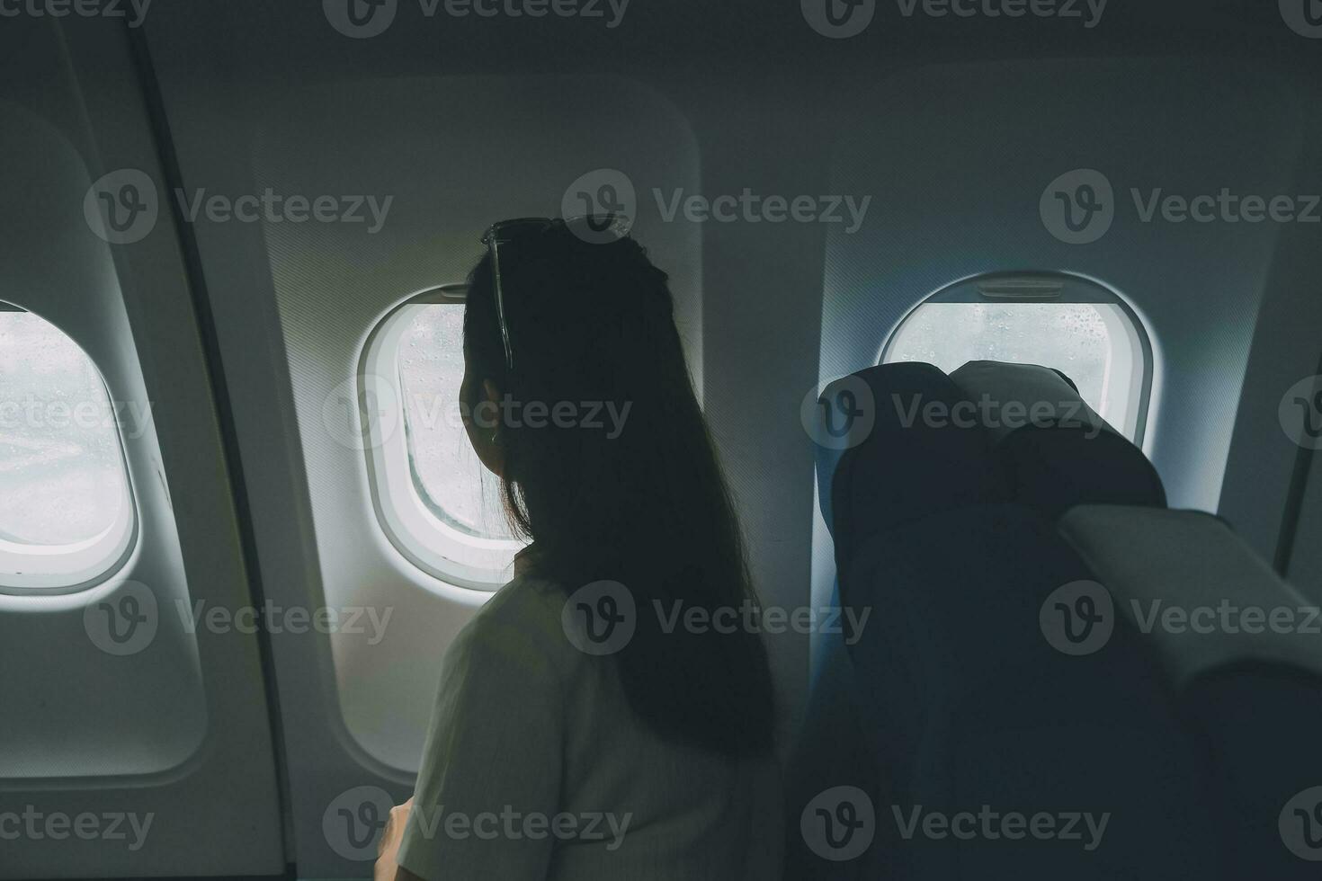 Silhouette of woman looks out the window of an flying airplane. Passenger on the plane resting beside the window. photo