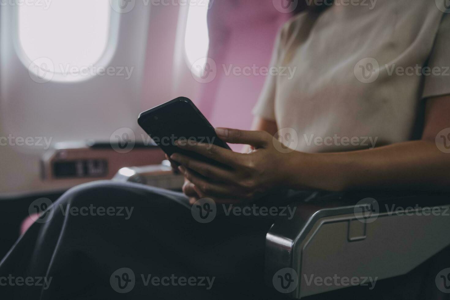 Asian woman passenger sitting in airplane near window and reading news from social networks or using travel applications in smartphone photo