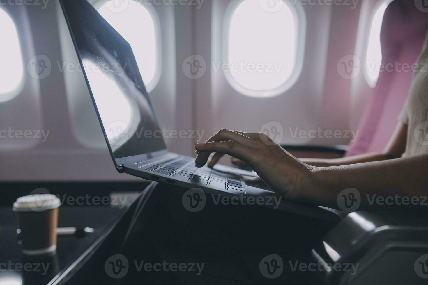 Asian woman passenger sitting in airplane near window and reading news from social networks or using travel applications in smartphone photo