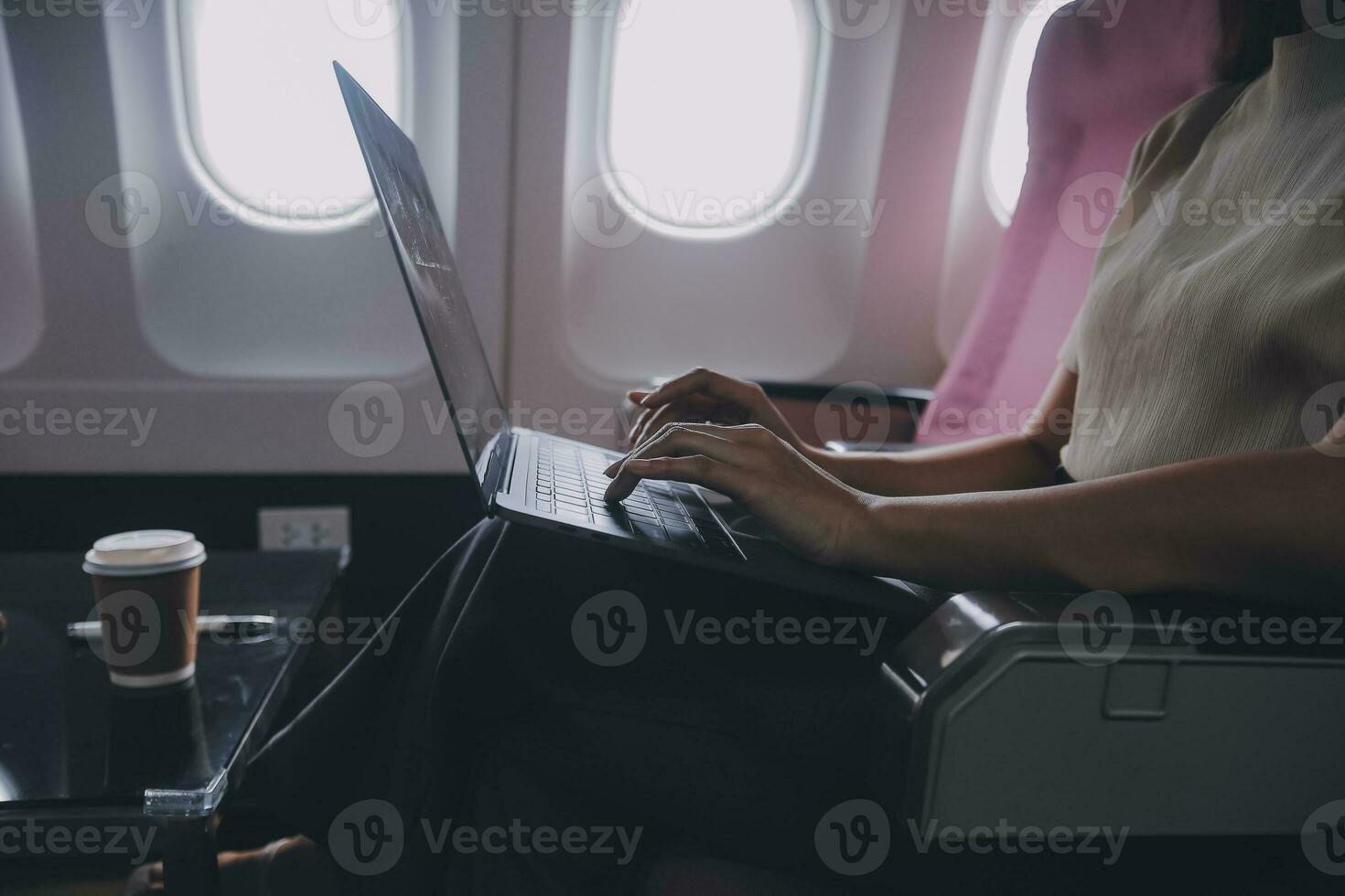Asian woman passenger sitting in airplane near window and reading news from social networks or using travel applications in smartphone photo