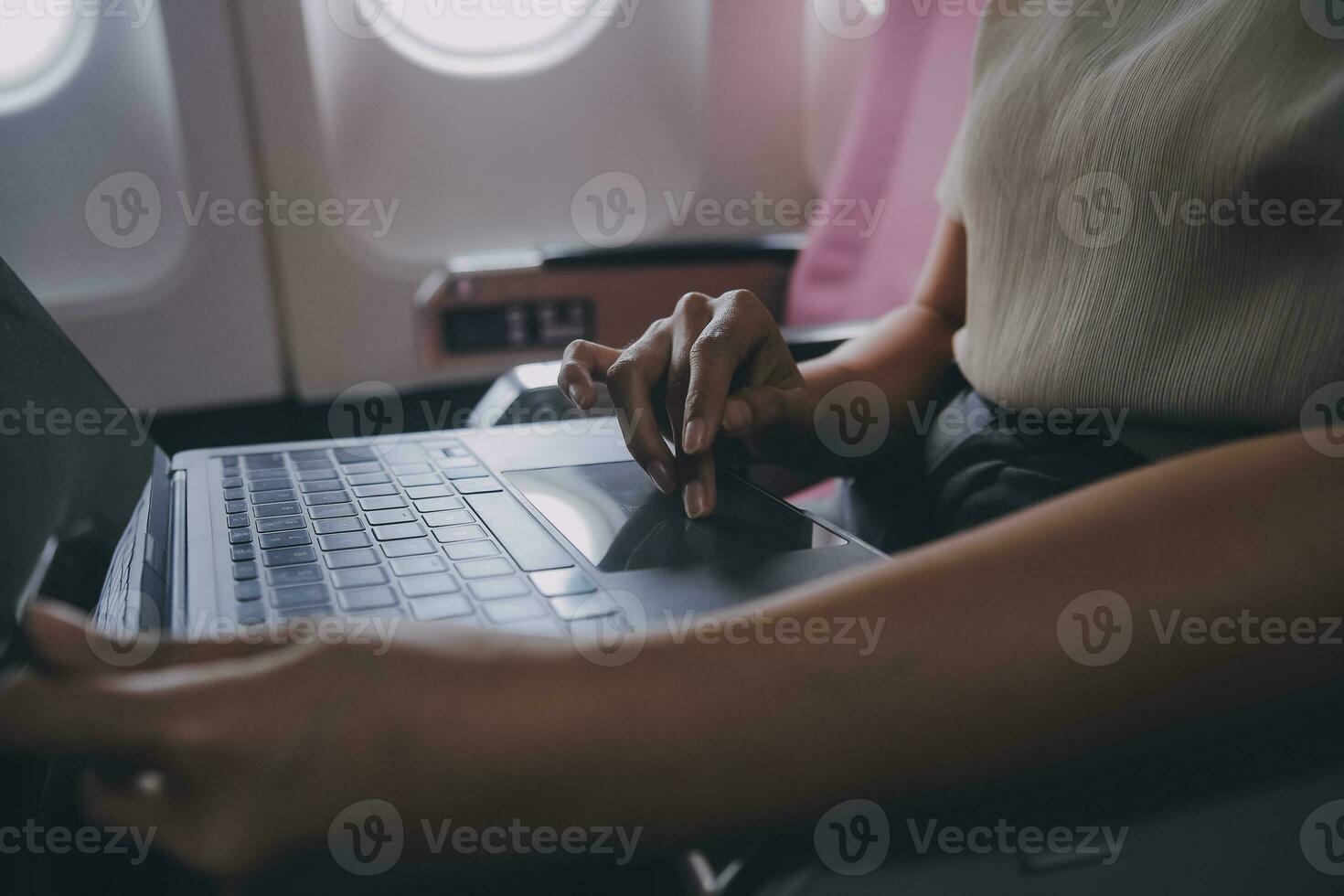 Asian woman passenger sitting in airplane near window and reading news from social networks or using travel applications in smartphone photo