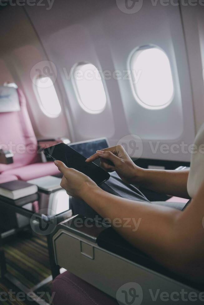 Asian woman passenger sitting in airplane near window and reading news from social networks or using travel applications in smartphone photo