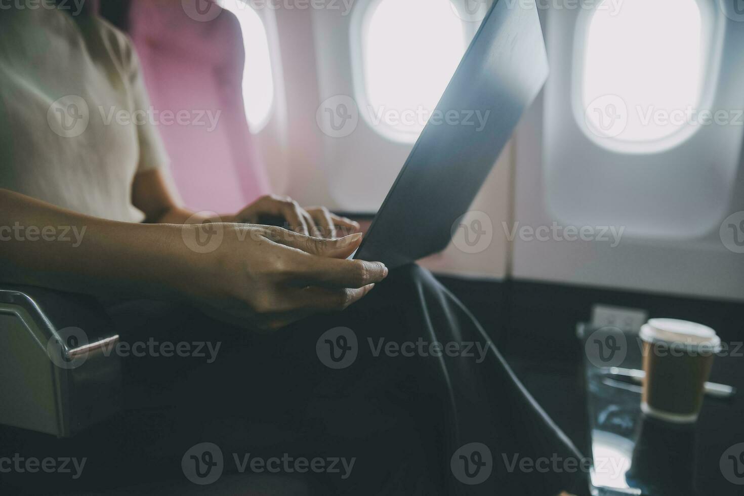 Asian woman passenger sitting in airplane near window and reading news from social networks or using travel applications in smartphone photo