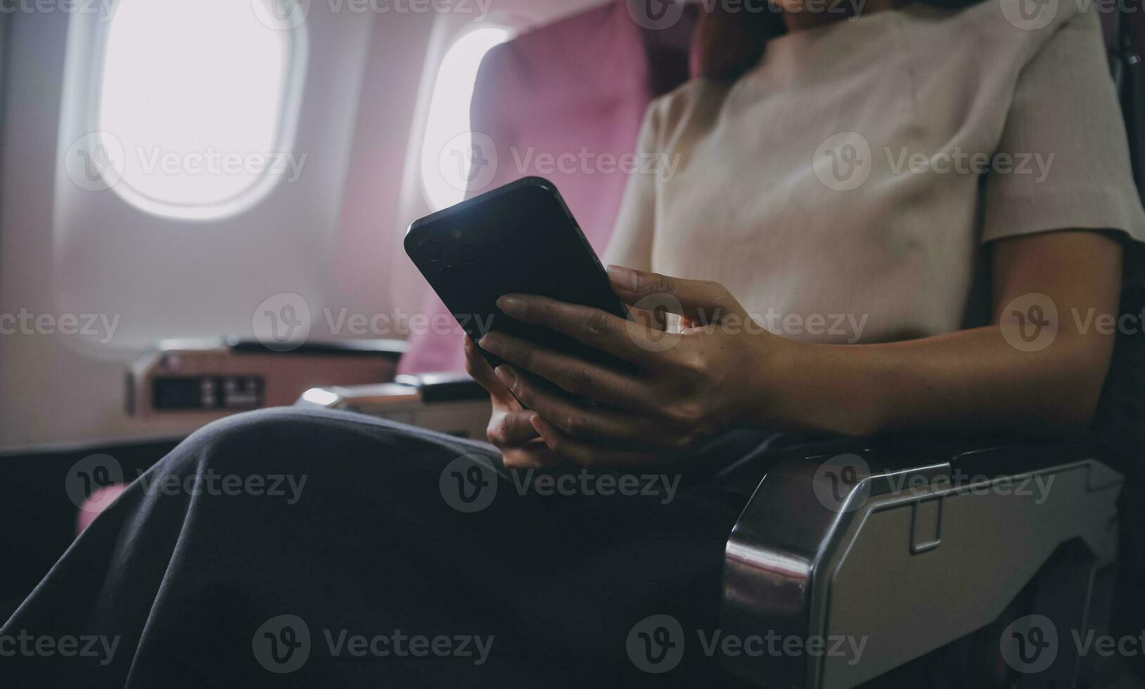 Asian woman passenger sitting in airplane near window and reading news from social networks or using travel applications in smartphone photo