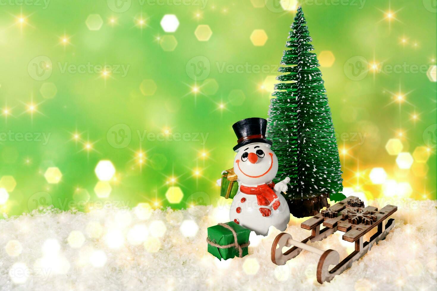 Cheerful snowman with a wooden sleigh and a Christmas tree on artificial snow and a green background with bokeh. New Year, Christmas, Christmas Eve photo