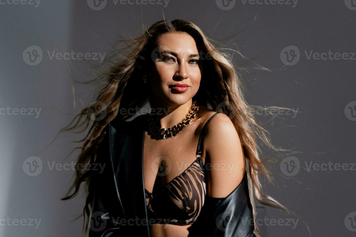 Model with luxurious hair flowing from a gust of wind in a black raincoat and seductive lingerie photo