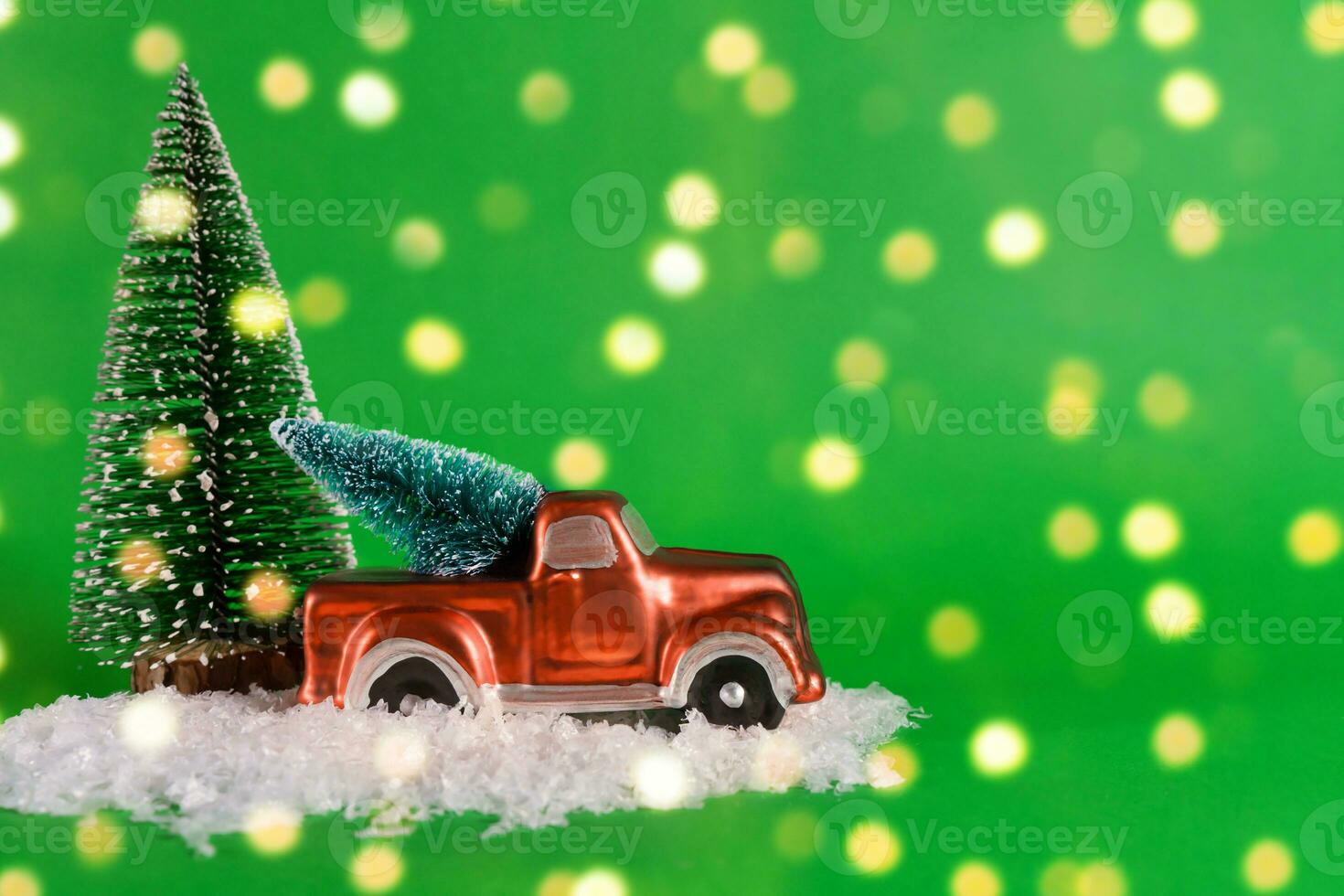 A red pickup truck is carrying a Christmas tree with artificial snow on a green background with bokeh. Banner, New Year card with copy space photo