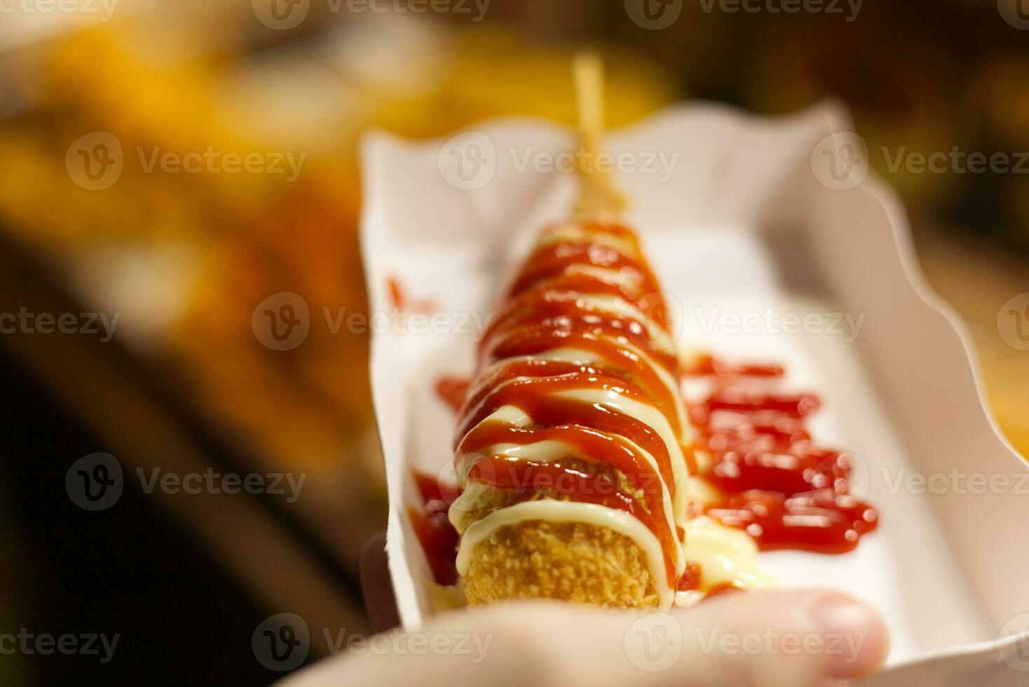 street food fried corn dog , battered sausage with mayonnaise,  tomato sauce on paper plate hold in hand photo