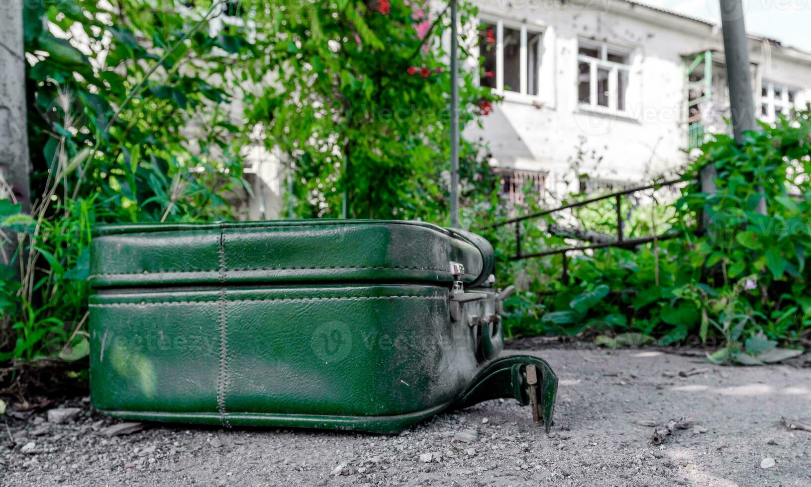old suitcase against the background of a destroyed house in an abandoned city in Ukraine photo