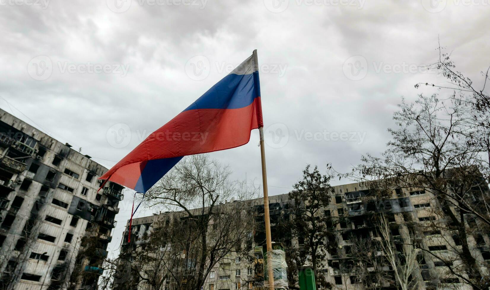 tricolor flag of Russia against the background of destroyed and burnt houses in Ukraine photo