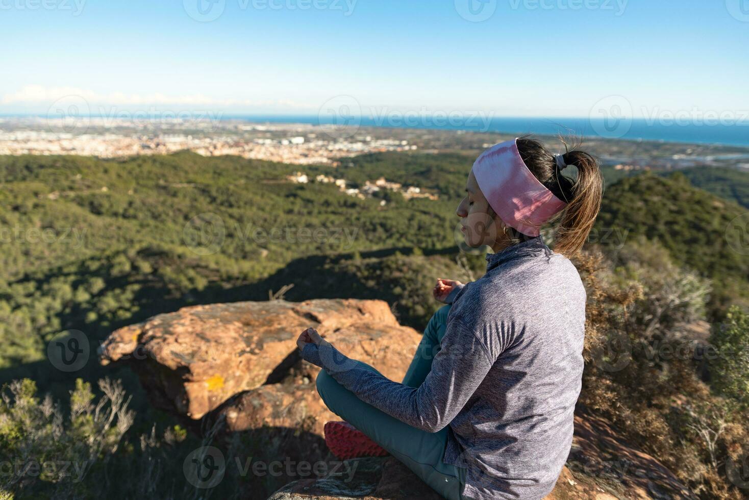Woman doing meditation on top of a mountain and surrounded by a natural environment. photo