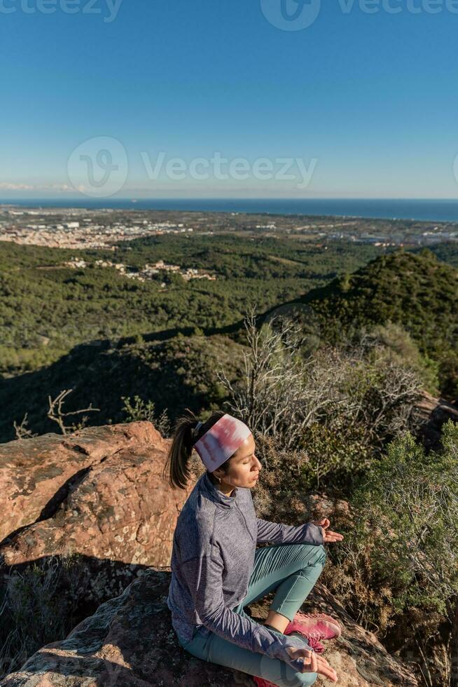 Woman doing meditation on top of a mountain and surrounded by a natural environment. photo