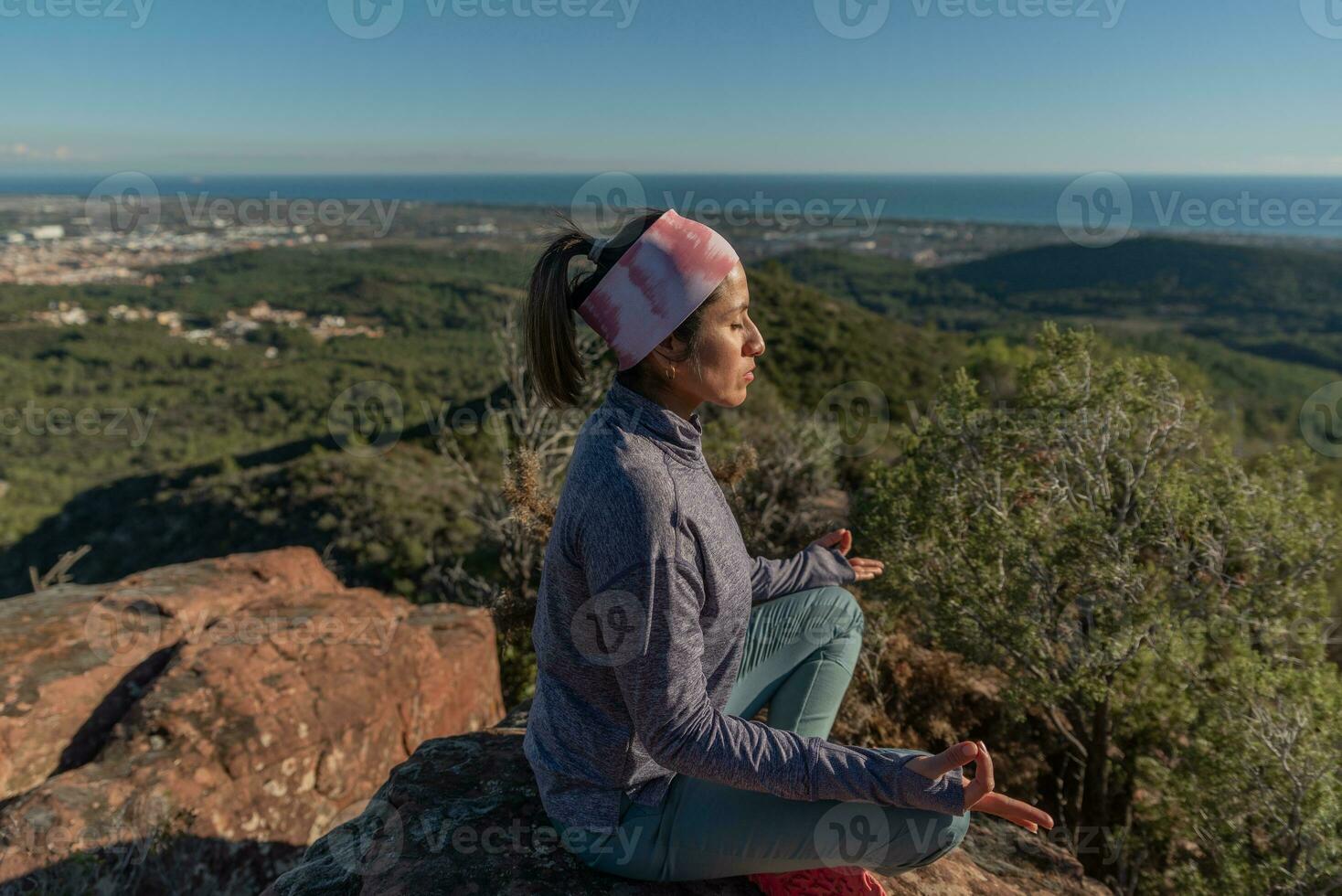 Woman doing meditation on top of a mountain and surrounded by a natural environment. photo