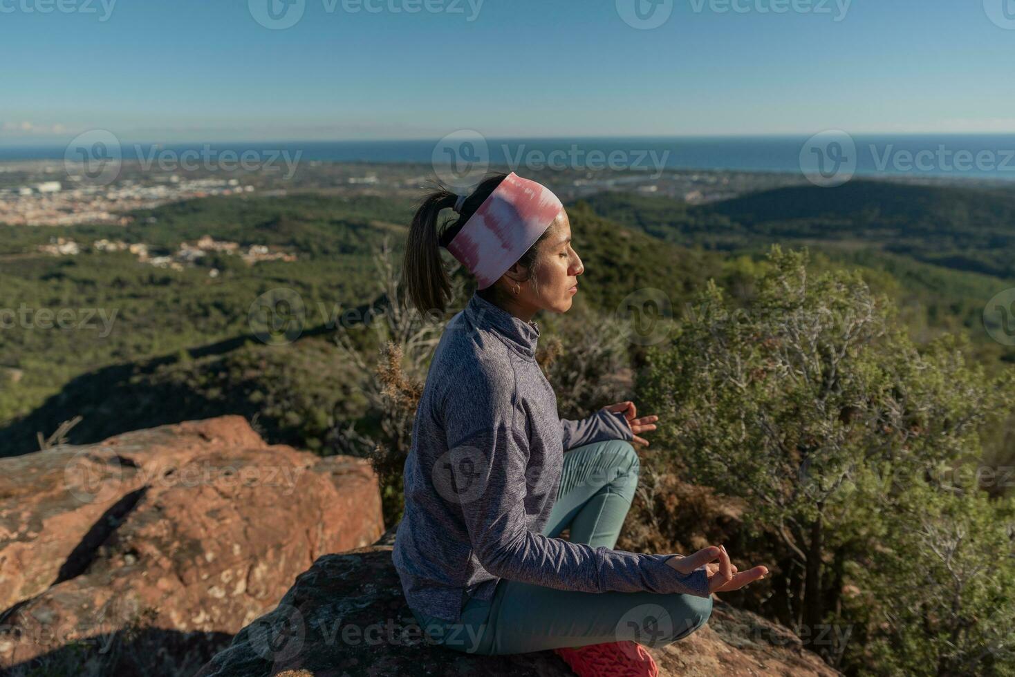 Woman doing meditation on top of a mountain and surrounded by a natural environment. photo