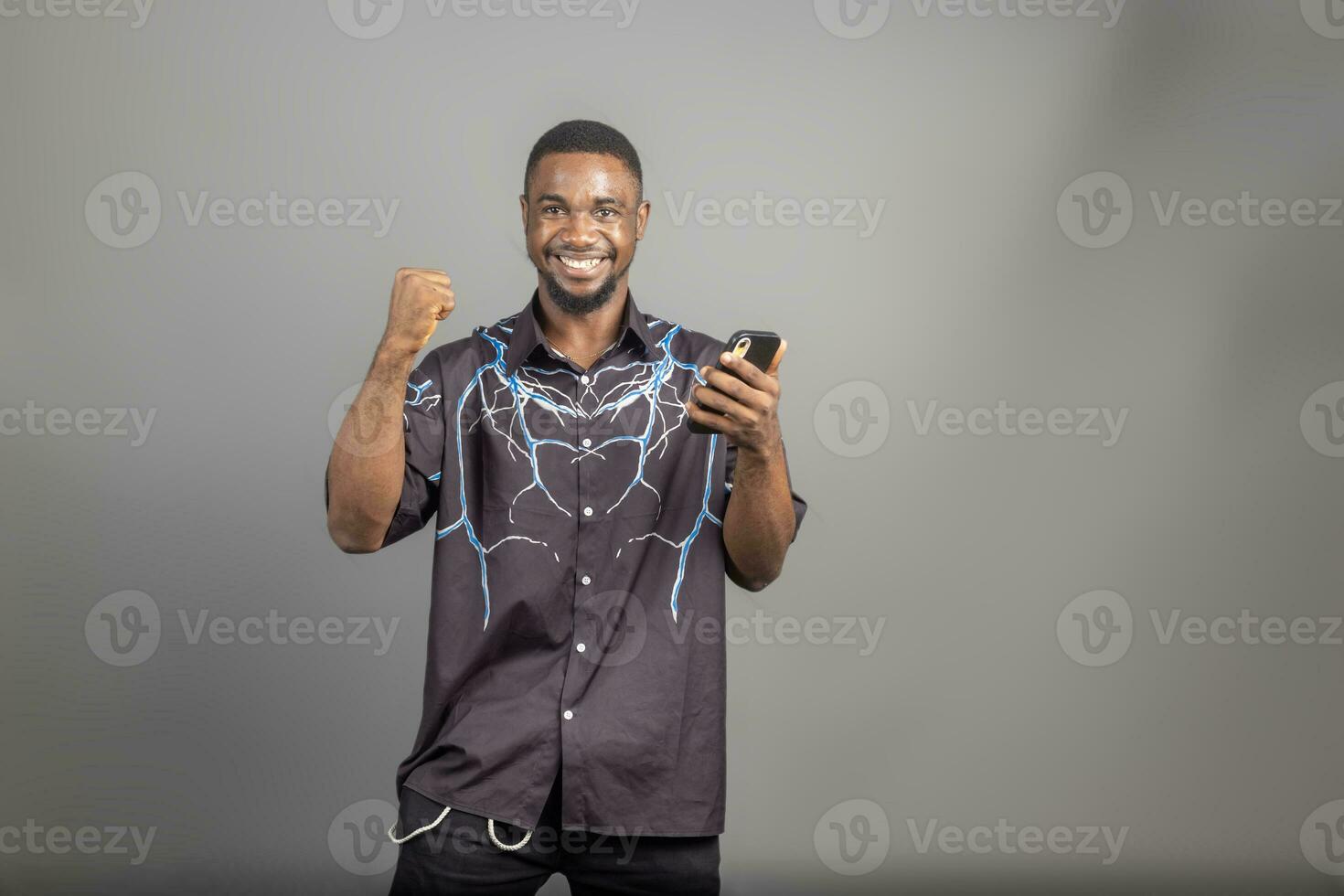 Cheerful millennial black man in casual using modern smart phone, checking social media, looking at copy space for mobile application photo