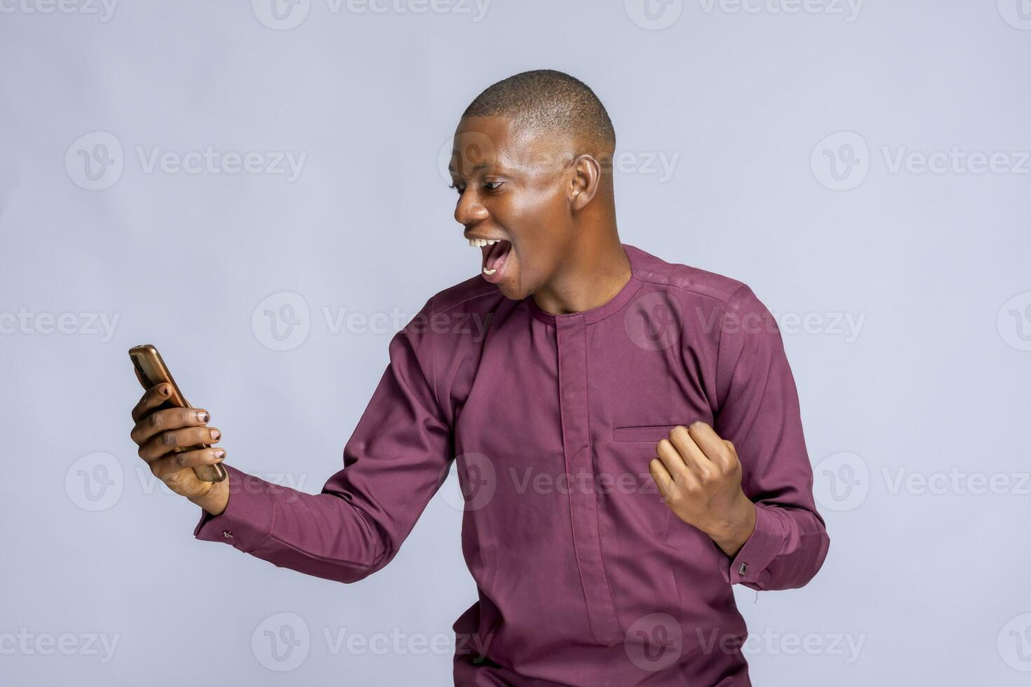 a young african man looking his cell phone with a raised fist photo