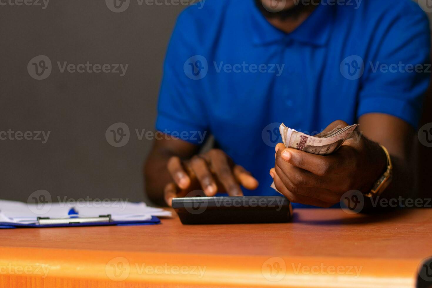young african man sitting at a desk holding some money and doing some calculations photo