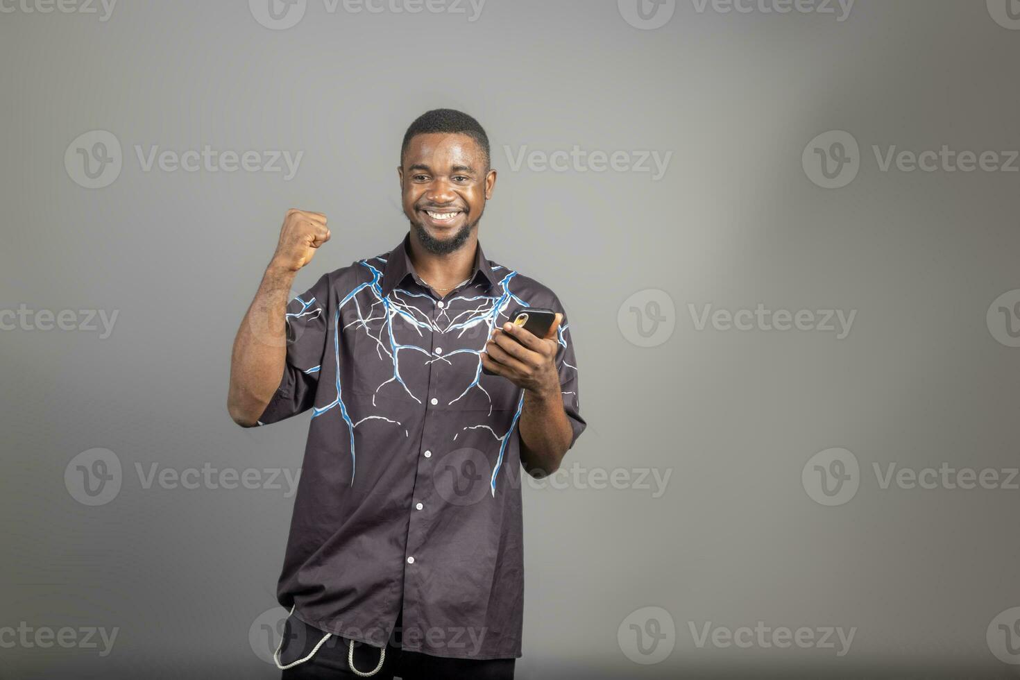 Cheerful millennial black man in casual using modern smart phone, checking social media, looking at copy space for mobile application photo