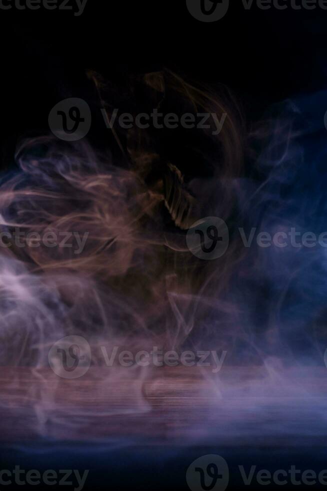 Conceptual image of multi-colored smoke isolated on dark black background and wooden table. photo