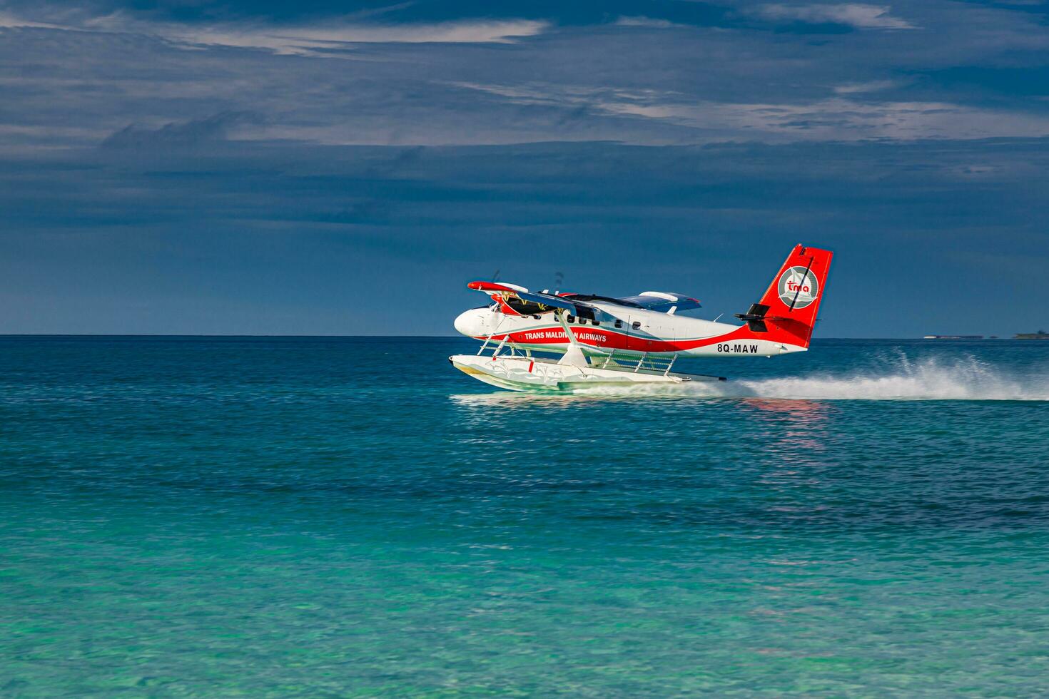 Twin otter red seaplane landing at Maldives. Luxury travel transportation in tropical Maldivian ocean lagoon. Exotic summer destination scenic. South Ari Atoll, Dhidhoofinolhu, Maldives - 12.15.21 photo