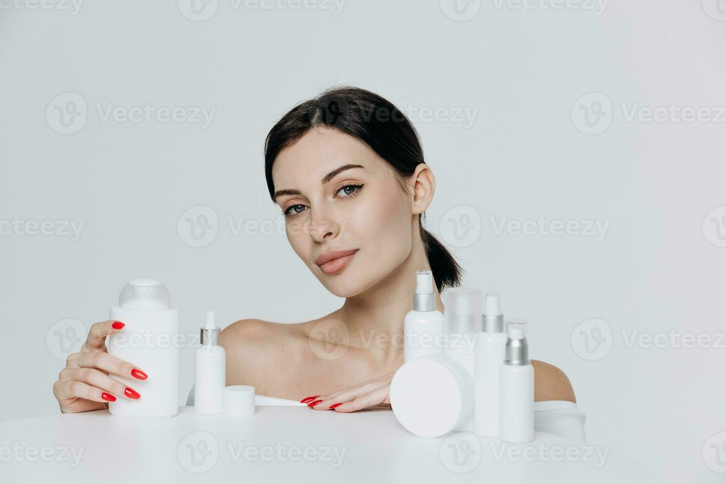 Beautiful young caucasian woman with perfect healthy skin proposing a product. Cosmetic bottles with a white label. Beauty blog, salon concept, minimalism brand packaging mockup photo