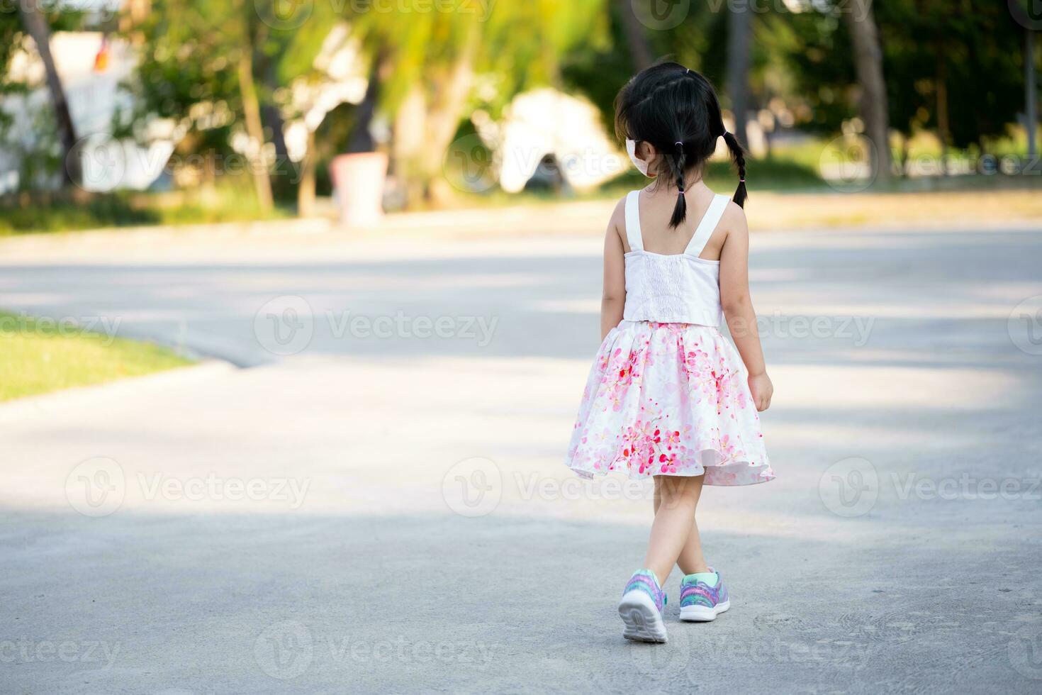 posterior espalda ver hermosa niño niña trotar en público parque en noche tiempo. verano o primavera tiempo. relajante niño vistiendo cara máscara para proteger untado virus y aire contaminación pm2.5. niños 5 5 año viejo. foto