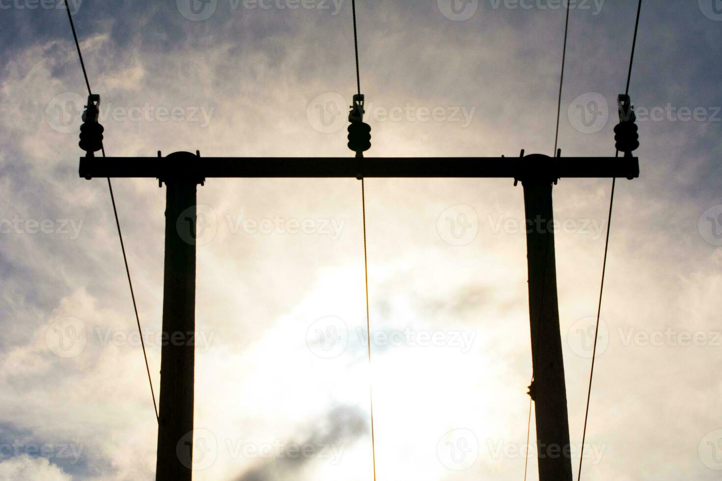 Wooden utility poles in silhouette with electricity wires on a cloudy sky during sunset. photo