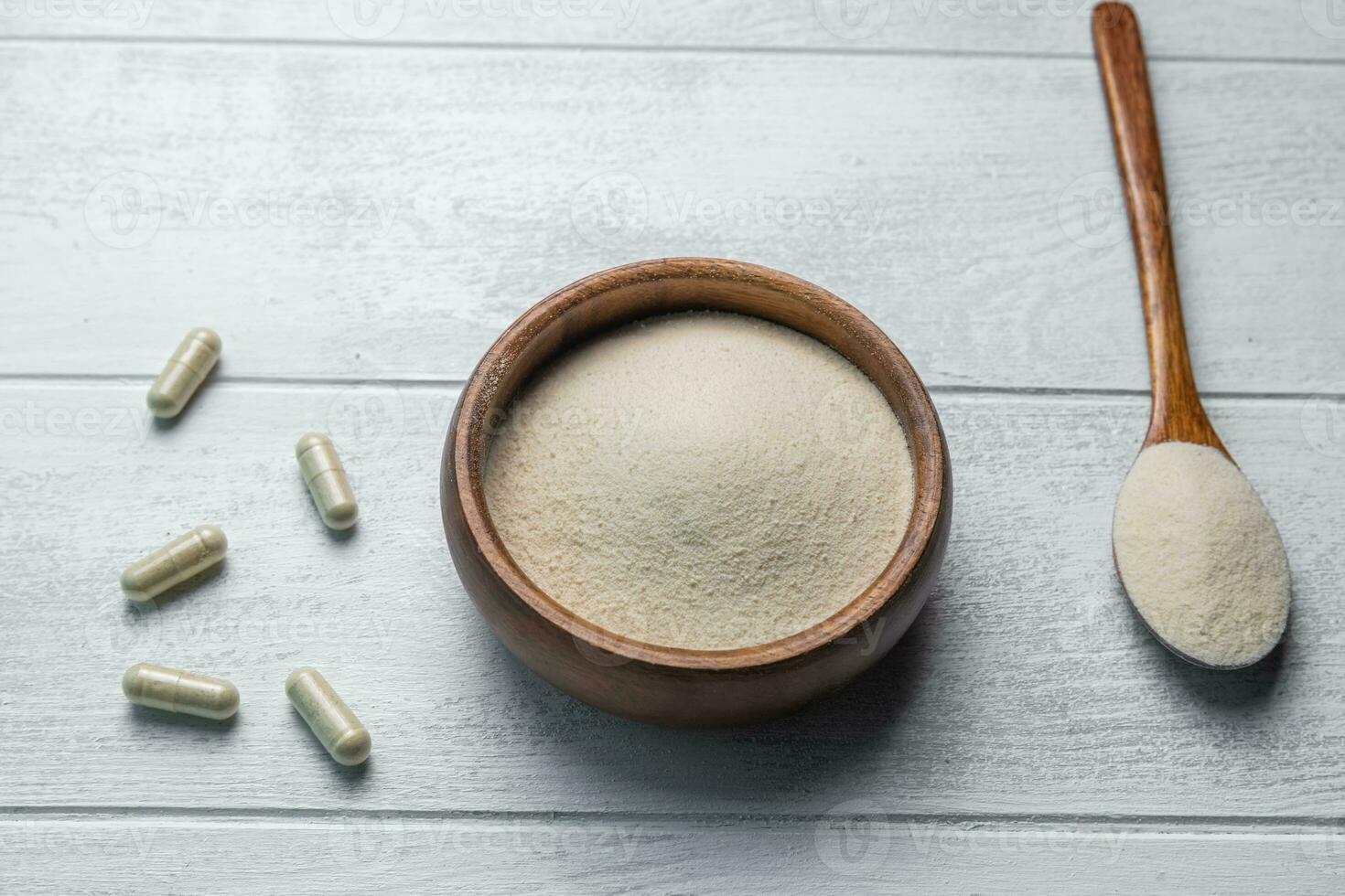 Collagen powder in bowl and spoon on wooden white background. photo