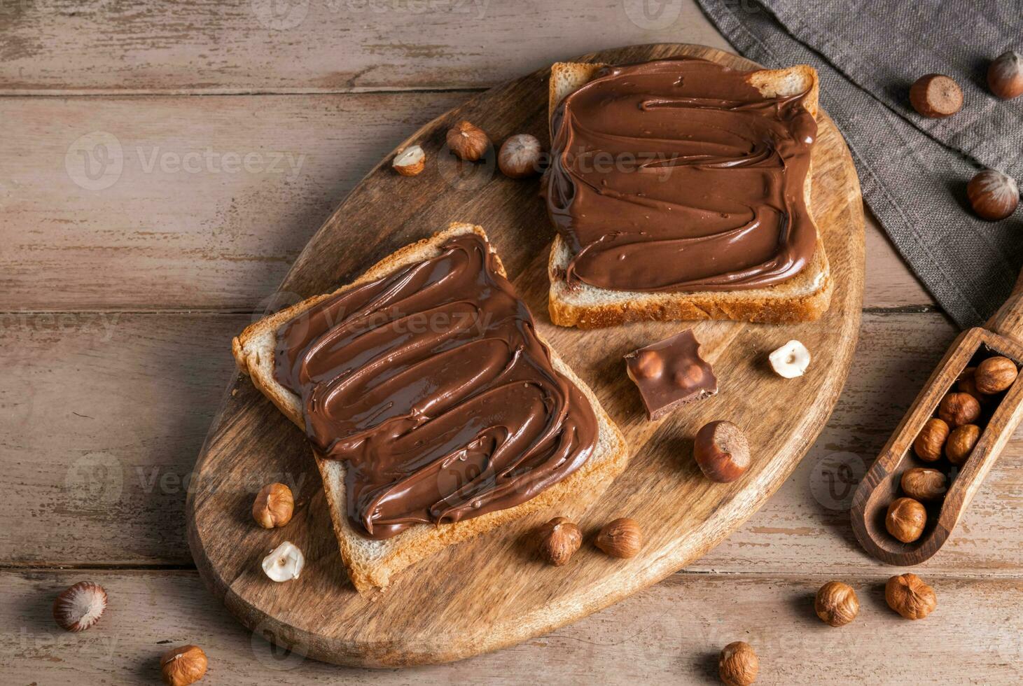 Board of bread with chocolate paste and hazelnuts on wooden background photo