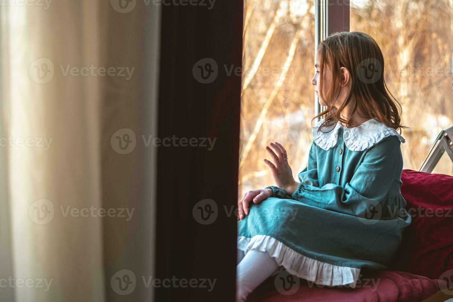 a pensive cute girl sits and looks out the window photo