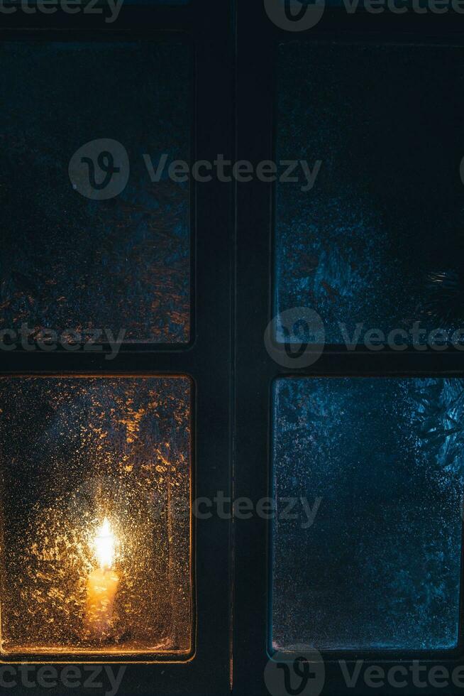 Christmas, new year, winter composition. Candle behind a frozen window photo