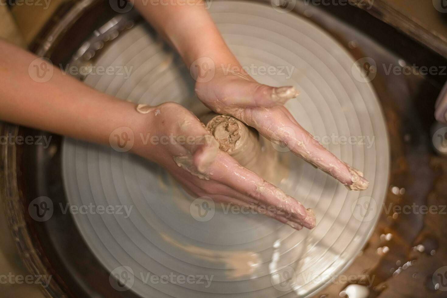 Potter girl works on potter's wheel, making ceramic pot out of clay in pottery workshop photo