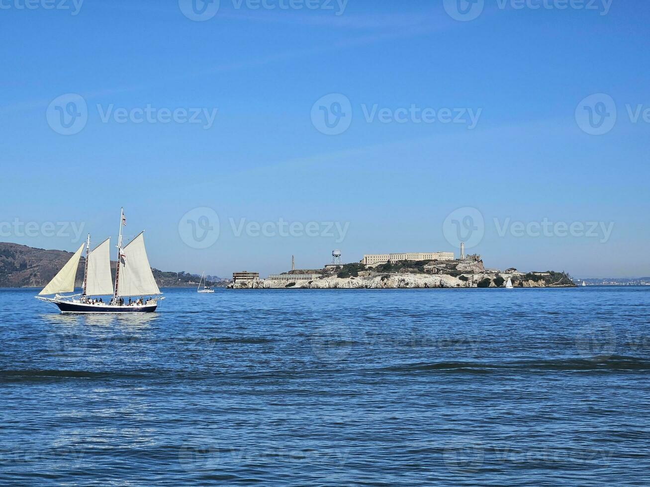 A sail boat crossing in front of Alcatraz Island in San Francisco California photo