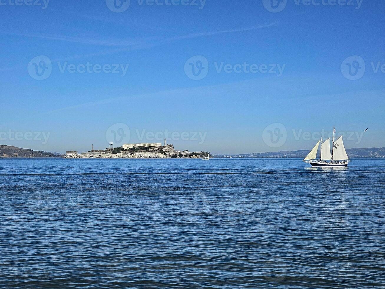 A sail boat crossing in front of Alcatraz Island in San Francisco California photo