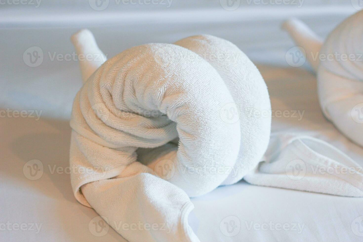 White towels on the bed in the hotel room are rolled up into the shape of an elephant's head. Soft, vintage tones. photo