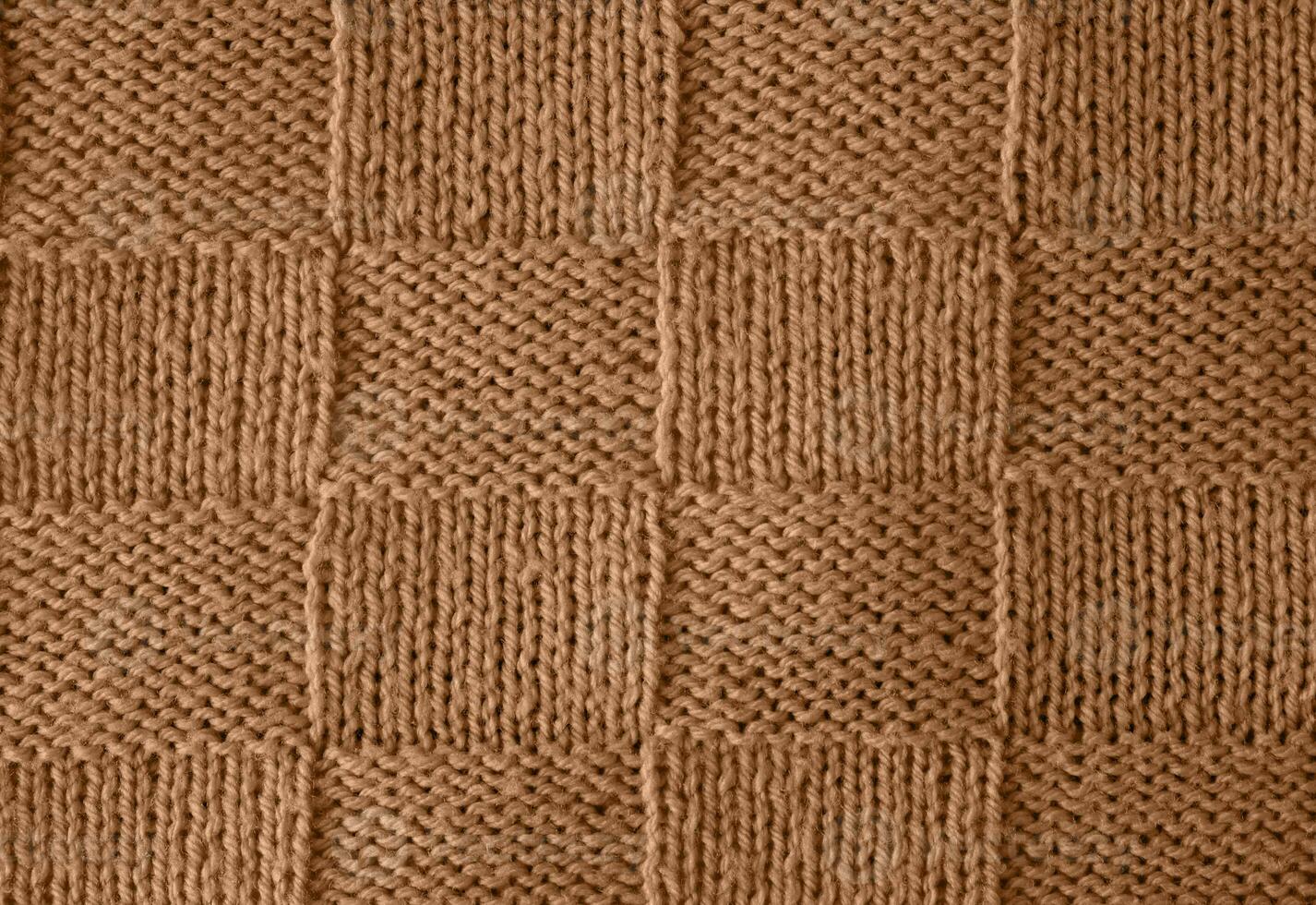 Texture of smooth knitted sweater with pattern. Handmade knitting wool or cotton fabric texture. Unusual abstract knitted chess pattern background texture. Peach Fuzz colour of 2024 year photo