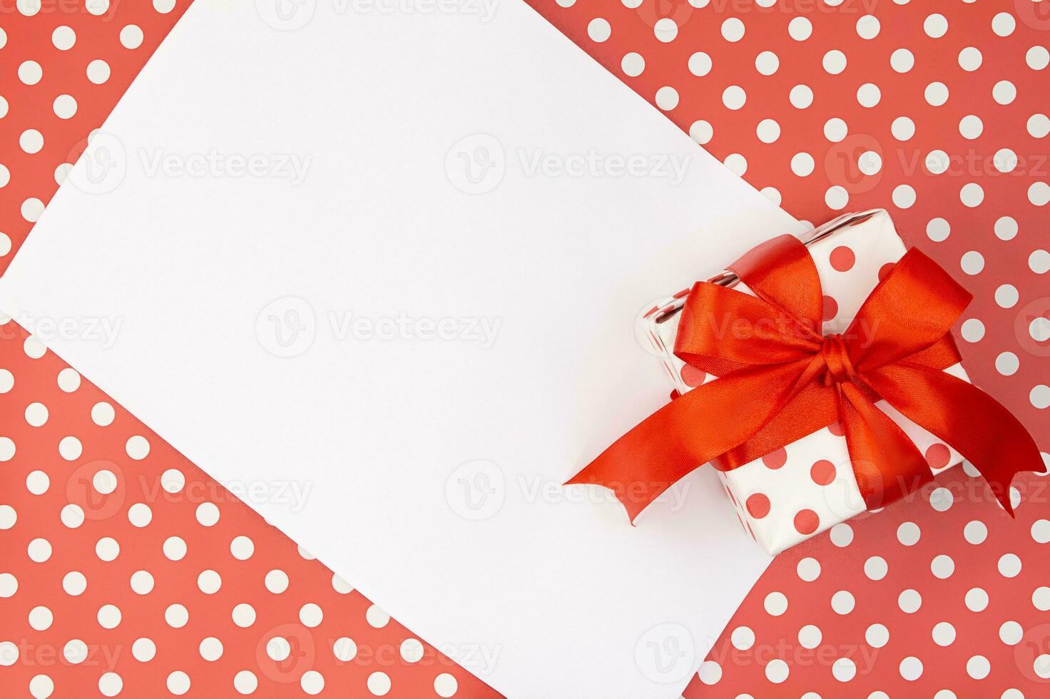 Red polka dots gift or present box with bow with paper on pattern background. Birthday, Valentine's, Mothers's and Women's day, holiday. Copy space photo