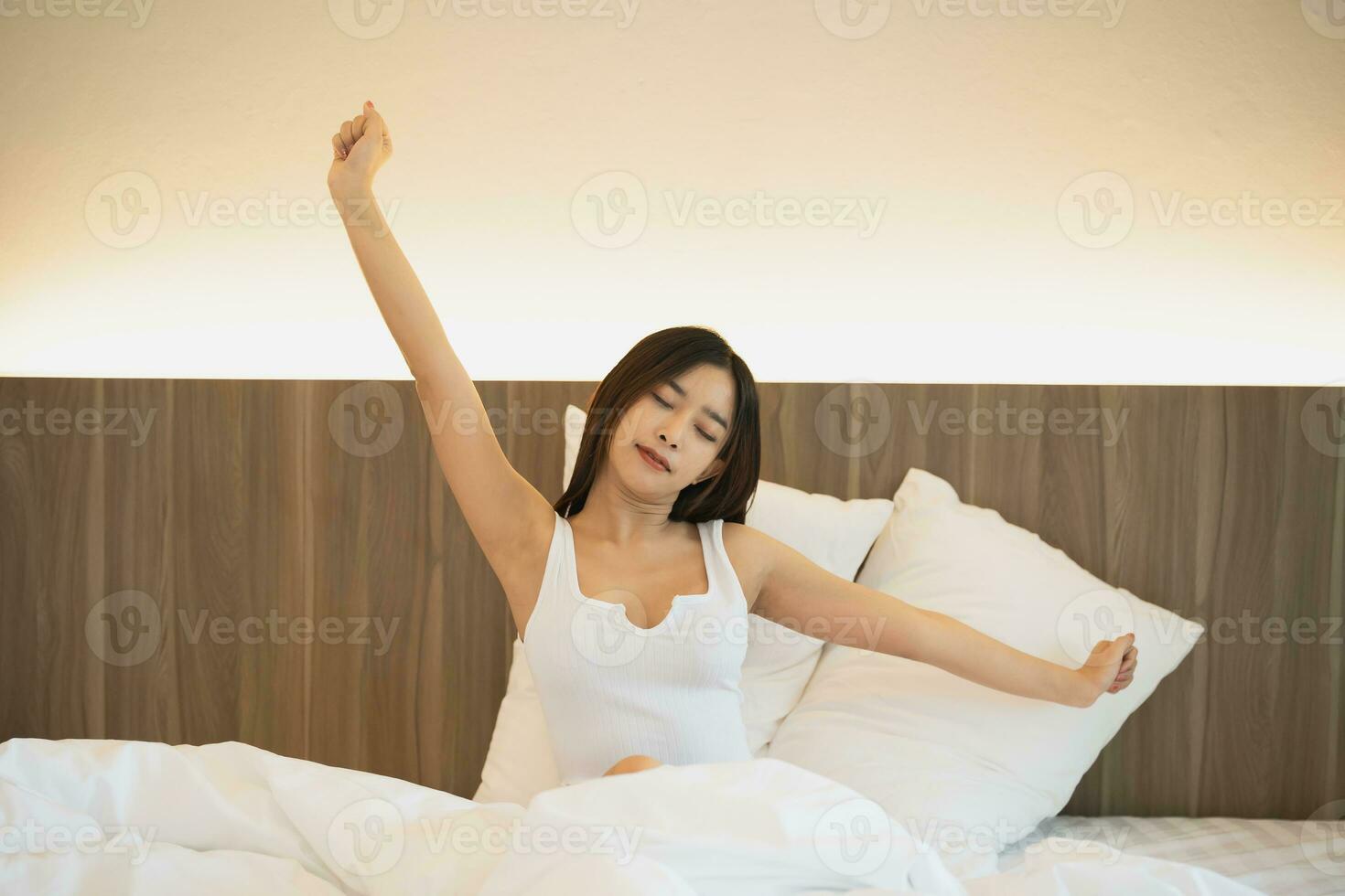 Asian woman laying on the bed, stretching and happy woman waking up in the morning after sleep, rest and relax at home. Resting, smile and stretch in bedroom, peaceful, cheerful comfortable concept. photo