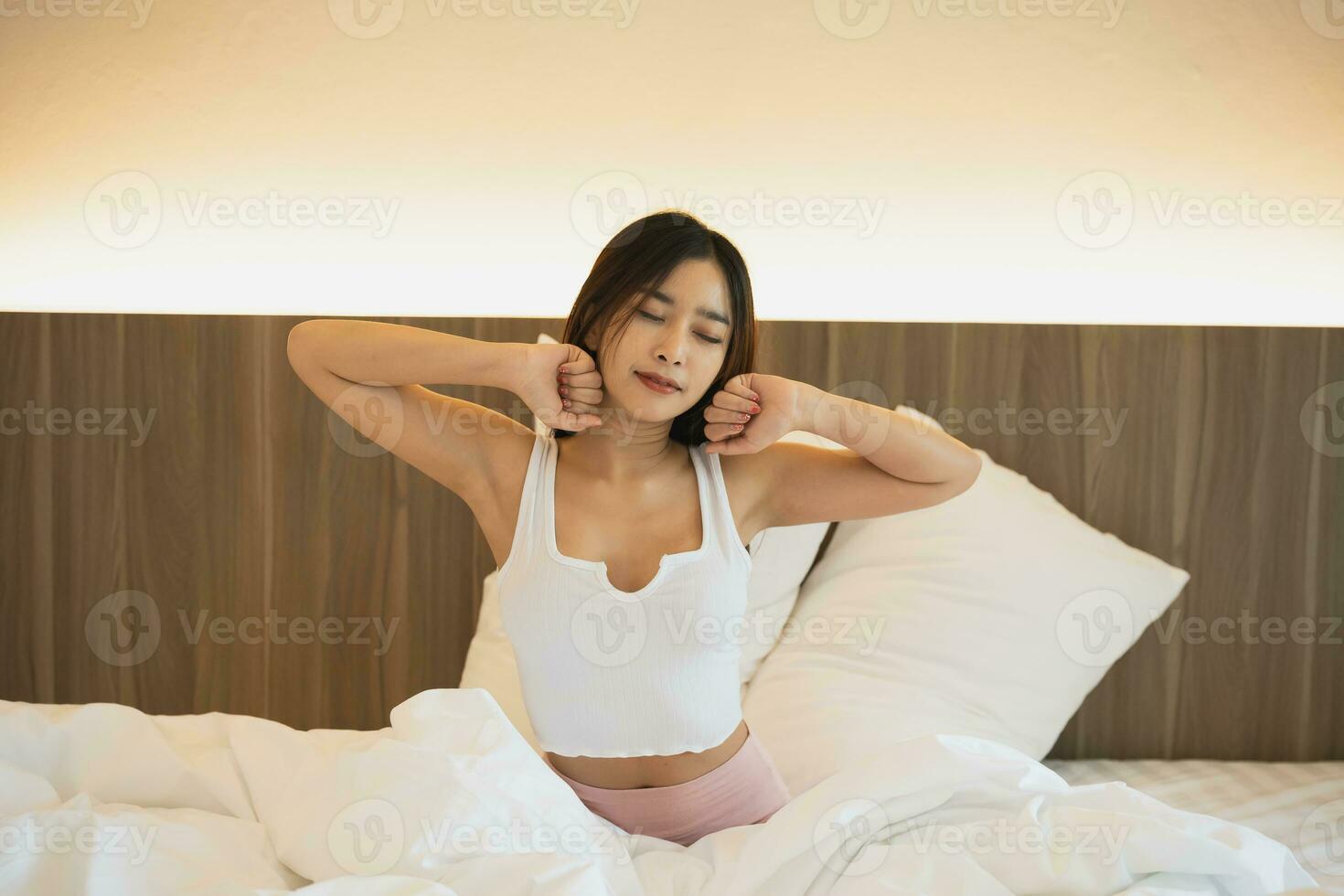 Asian woman laying on the bed, stretching and happy woman waking up in the morning after sleep, rest and relax at home. Resting, smile and stretch in bedroom, peaceful, cheerful comfortable concept. photo